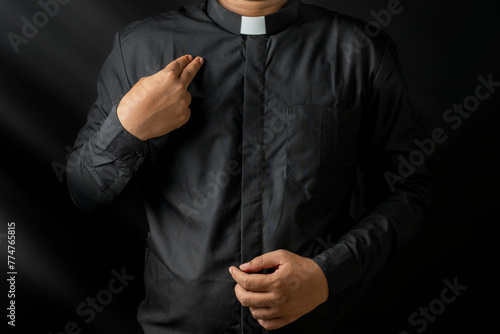 Young priest doing cross sign on his body isolated on black background.