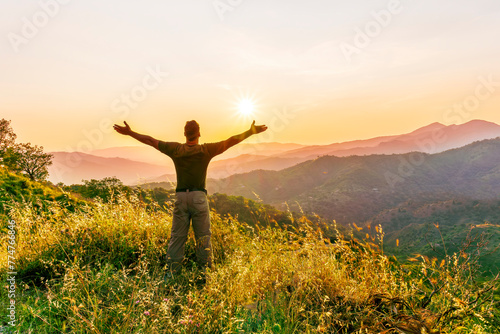 rejoicing man with beautiful scenic mountain sunset landscape on background. happy man watching amazing evening sunset © Yaroslav
