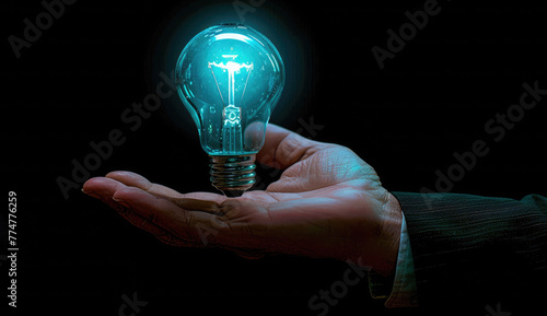 A hand holds a glowing light bulb symbolizing innovation and creative thinking for business concepts against a black background. A businessman in a suit holds his hand out to a digital virtual icon