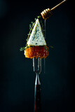 Blue cheese with honey on a fork. Honeycombs. On a black background. Creative photo.