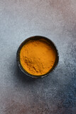 Spices. Turmeric powder in a black ceramic bowl on a concrete gray background.