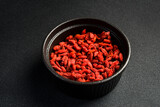 Close up of red dried goji berries in a bowl. On a dark concrete background.