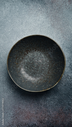 Ceramic dark round textured plate. Close up on gray concrete background. Free space for text.