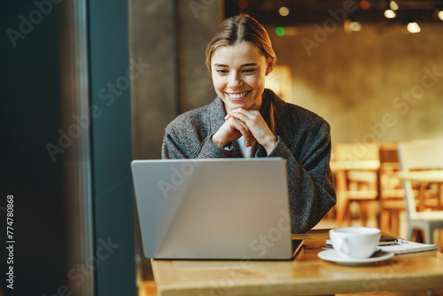 Pretty young female freelancer working on laptop while sitting in cozy cafe 