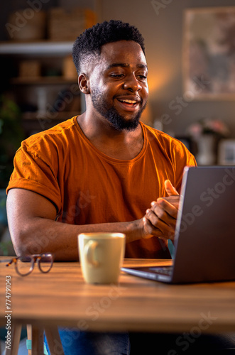 Smiling young African American man sitting at home using laptop for video call.