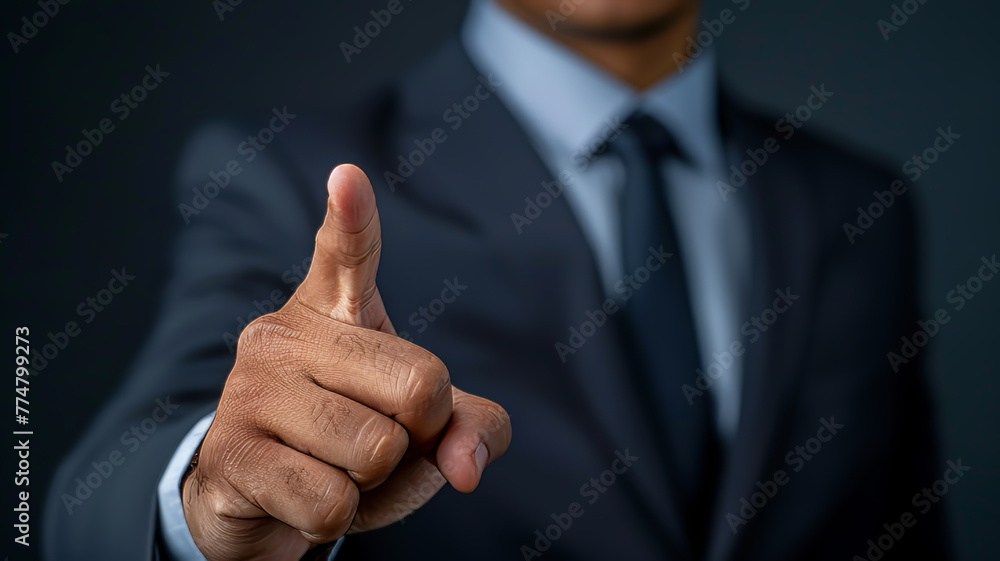 Close-up of a businessman's hand showing a thumbs up sign or forefinger , with a dark, blurred background. Close-up of a businessman's hand showing a thumbs up sign or forefinger , with a dark, blurred background.