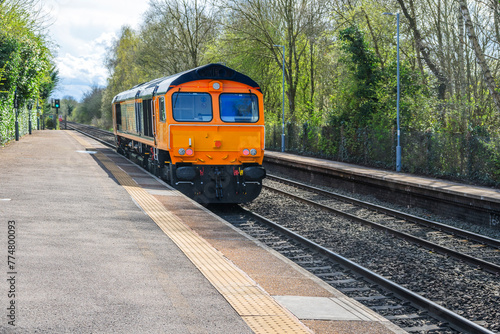 Freight train passing through English rural country passenger commuter station, West Midlands England UK.
