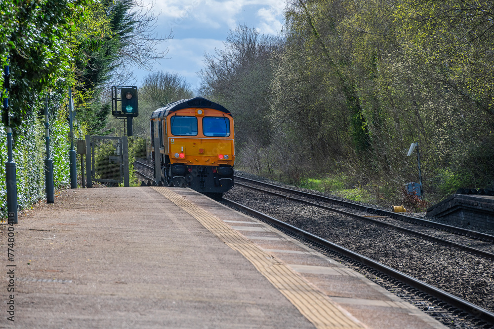 Naklejka premium Freight train passing through English rural country passenger commuter station, West Midlands England UK.