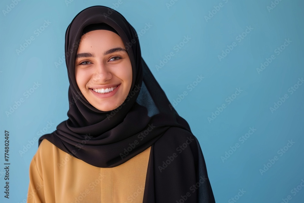 Portrait of young smiling Arabian muslim woman in black hijab on blue background with copy space Portrait of young smiling Arabian muslim woman in black hijab on blue background with copy space