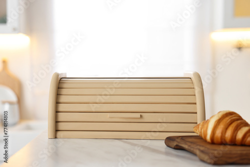 Wooden bread box and board with croissant on white marble table in kitchen