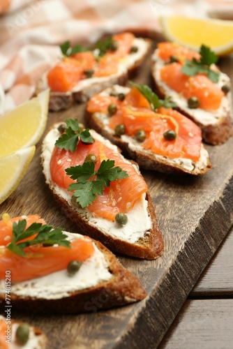 Tasty canapes with salmon, capers, lemon and cream cheese on wooden table, closeup