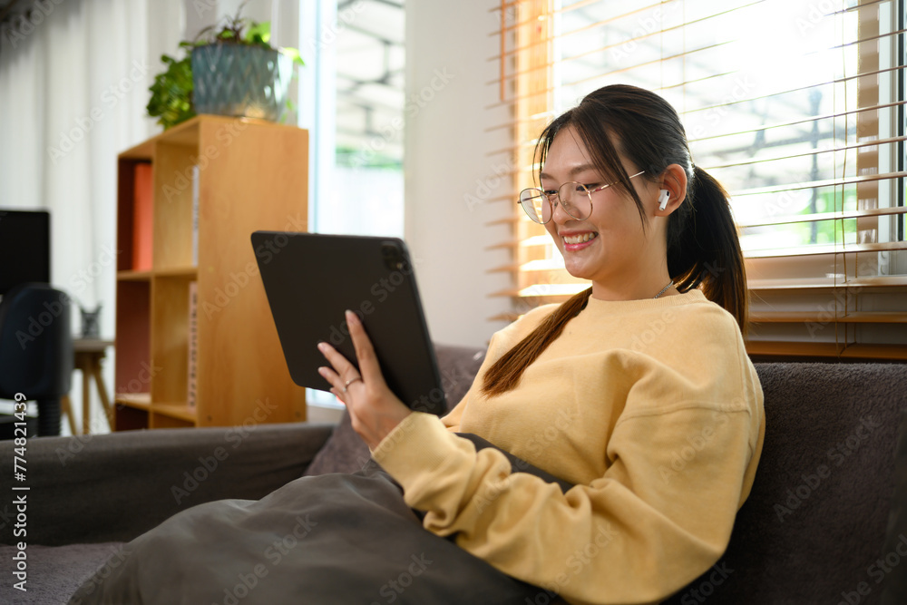 Smiling young woman in eyeglasses watching video on digital tablet at home Smiling young woman in eyeglasses watching video on digital tablet at home