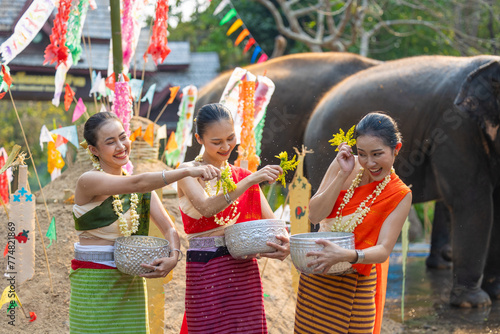 Songkran festival. Northern Thai people in Traditional clothes dressing splashing water together in Songkran day cultural festival with sand pagoda and colorful paper flag.