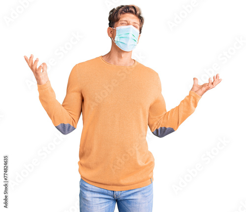 Young handsome man wearing medical mask crazy and mad shouting and yelling with aggressive expression and arms raised. frustration concept.