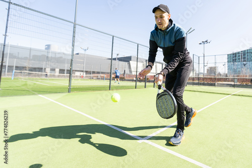 Man playing padel in a green grass padel court indoor behind the net © Angelov
