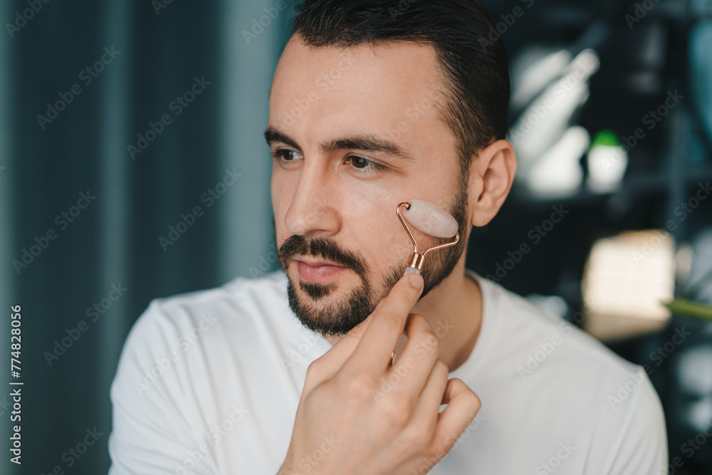 Portrait or a man with jade roller, facial product for soft or healthy skincare. Relaxing, dermatology cosmetics for face massage Portrait or a man with jade roller, facial product for soft or healthy skincare. Relaxing, dermatology cosmetics for face massage