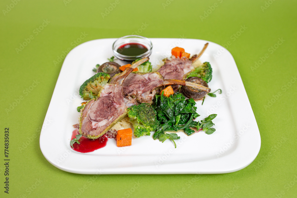 Lamb chops with vegetables on a white plate on a green background