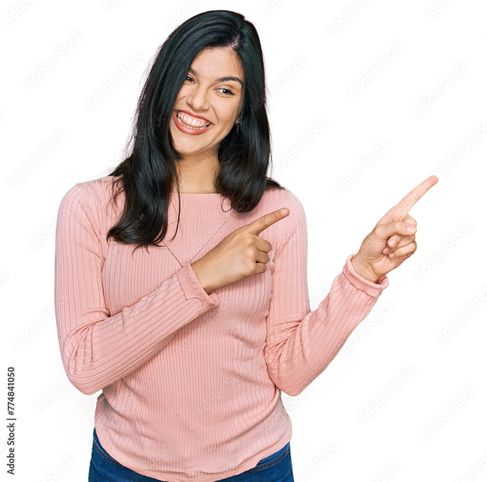Young hispanic woman wearing casual clothes smiling and looking at the camera pointing with two hands and fingers to the side.