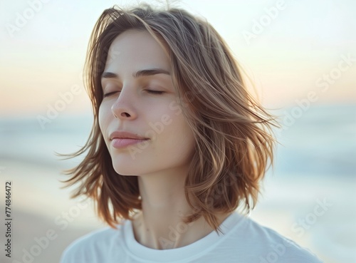 Close-up portrait of a beautiful woman with closed eyes and shoulder-length brown hair wearing a white t-shirt standing on the beach  copy space for text stock photo