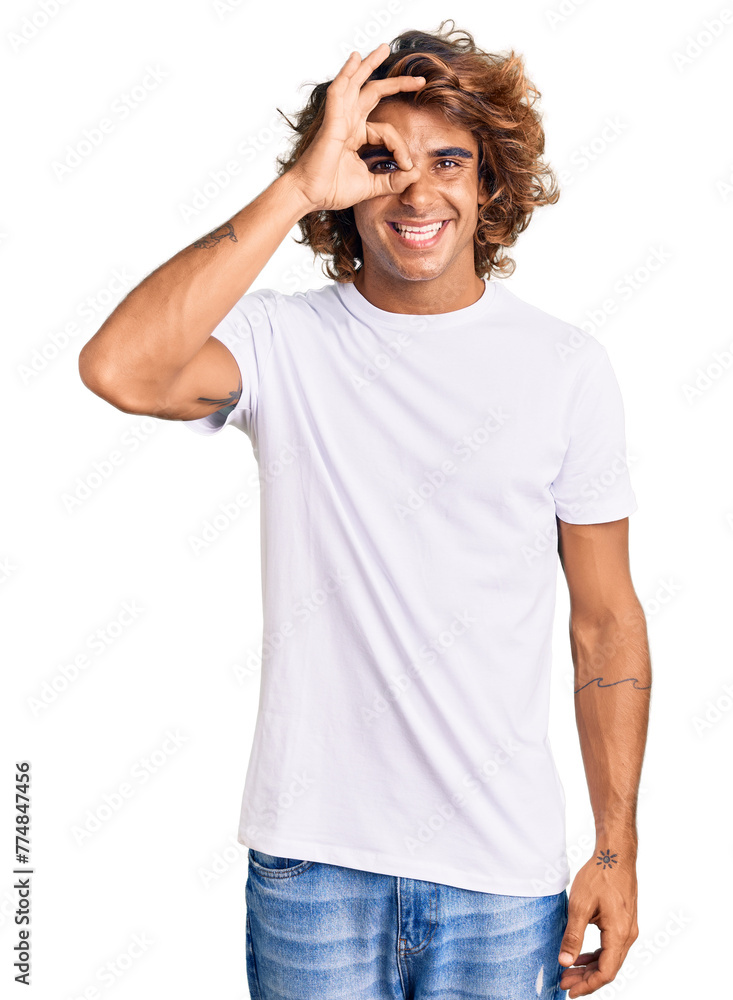 Young hispanic man wearing casual white tshirt doing ok gesture with hand smiling, eye looking through fingers with happy face. Young hispanic man wearing casual white tshirt doing ok gesture with hand smiling, eye looking through fingers with happy face.