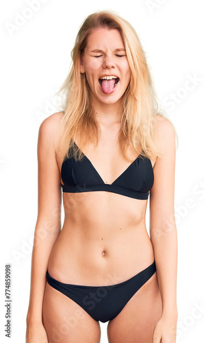 Young beautiful blonde woman wearing bikini sticking tongue out happy with funny expression. emotion concept. © Krakenimages.com