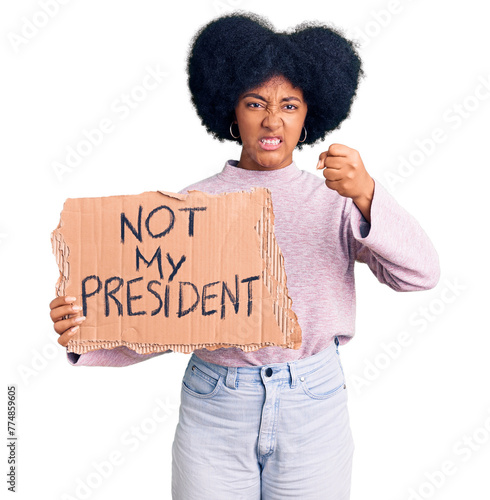Young african american girl holding not my president protest banner annoyed and frustrated shouting with anger, yelling crazy with anger and hand raised © Krakenimages.com