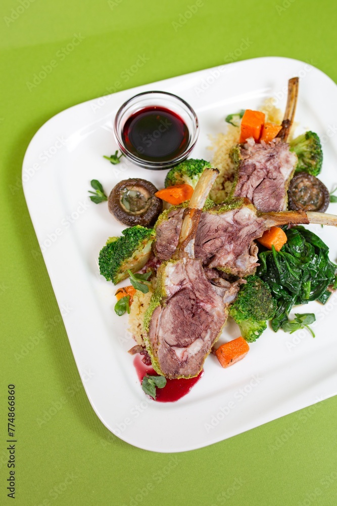 A delicious and healthy rib dish with mushrooms, broccoli, carrots and spinach on a white plate on a green background
