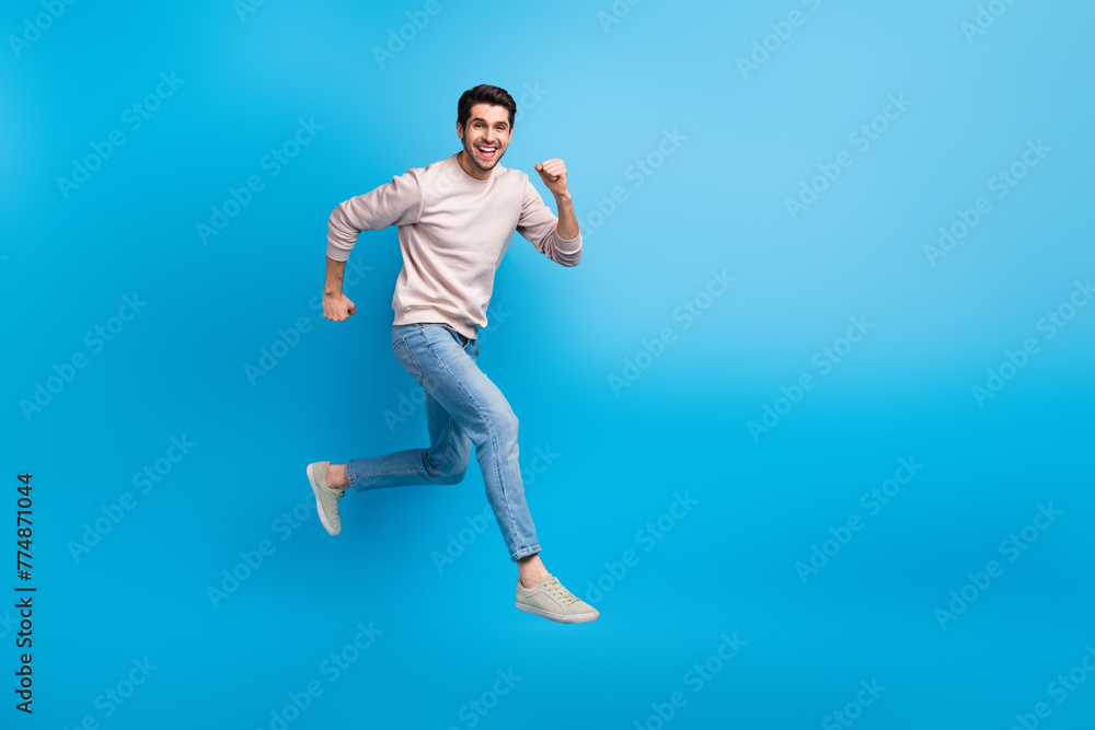 Fototapeta premium Full body portrait of nice young man jump run empty space wear beige sweatshirt isolated on blue color background