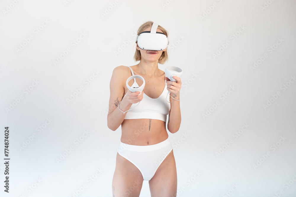 Beautiful thin girl in white shorts and a top in a virtual reality helmet posing on a white background