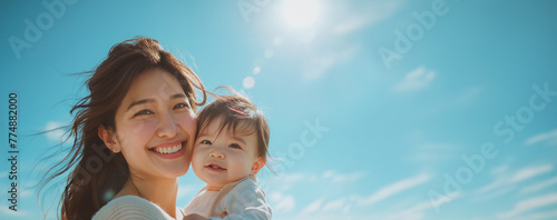 Portrait of joyful mother holds her smiling baby close, both basking in the sunlight under a clear blue sky, sharing a beautiful bonding moment. Love family Mother's Day concept photo