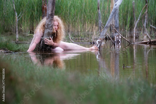 sexy nude lying mature red-haired woman as nymph mermaid in the water of Restloch 1332 behind dead tree trunks in Weißwasser, Oberlausitz, photo