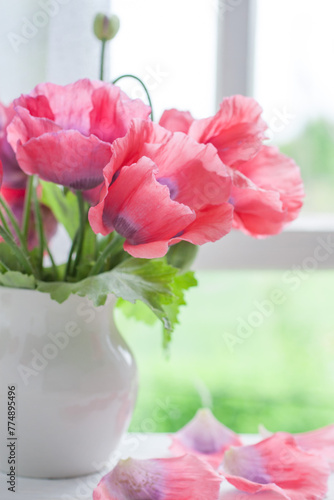 Blooming poppies in a white vase on a white wooden table near the window