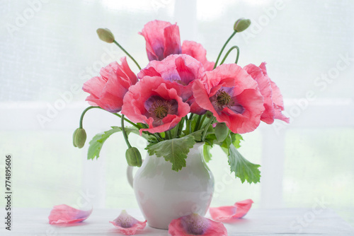 Blooming poppies in a white vase on a white wooden table near the window