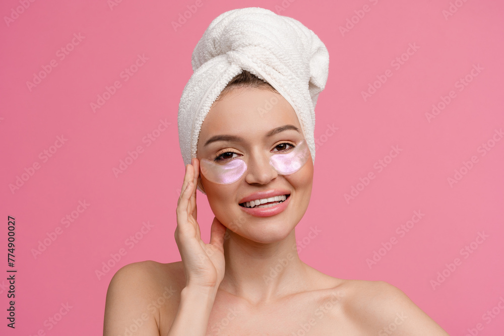 smiling h woman after shower on pink background with bath towel doing morning skincare routine using eye patches smiling h woman after shower on pink background with bath towel doing morning skincare routine using eye patches