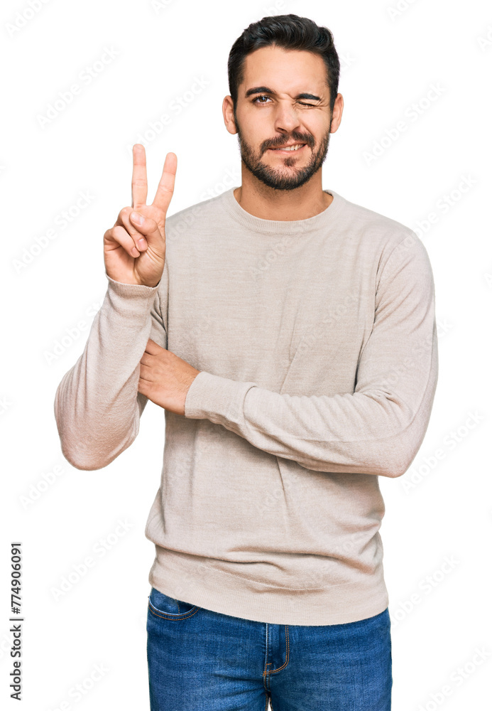 Fototapeta premium Young hispanic man wearing casual clothes smiling with happy face winking at the camera doing victory sign. number two.