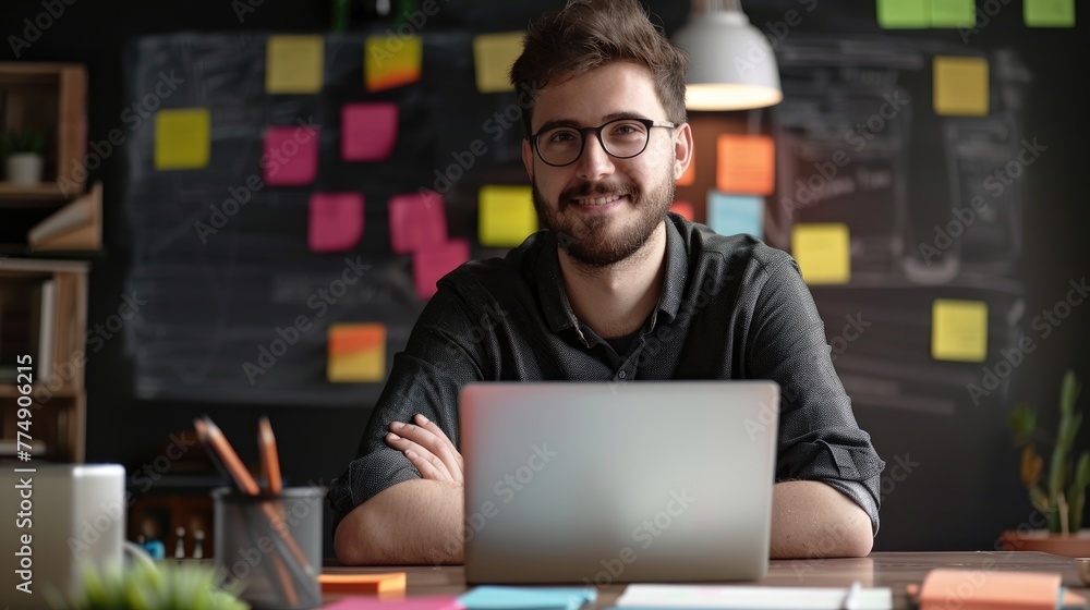 portrait of smiling young Arabian man working in a creative office, with a laptop and full of colorful sticky notes on a blackboard, Startup Project. portrait of smiling young Arabian man working in a creative office, with a laptop and full of colorful sticky notes on a blackboard, Startup Project.