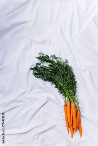 A bunch of carrots with greens on a white material
