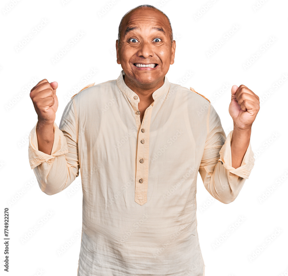 Hispanic middle age man wearing boho shirt celebrating surprised and amazed for success with arms raised and open eyes. winner concept. Hispanic middle age man wearing boho shirt celebrating surprised and amazed for success with arms raised and open eyes. winner concept.