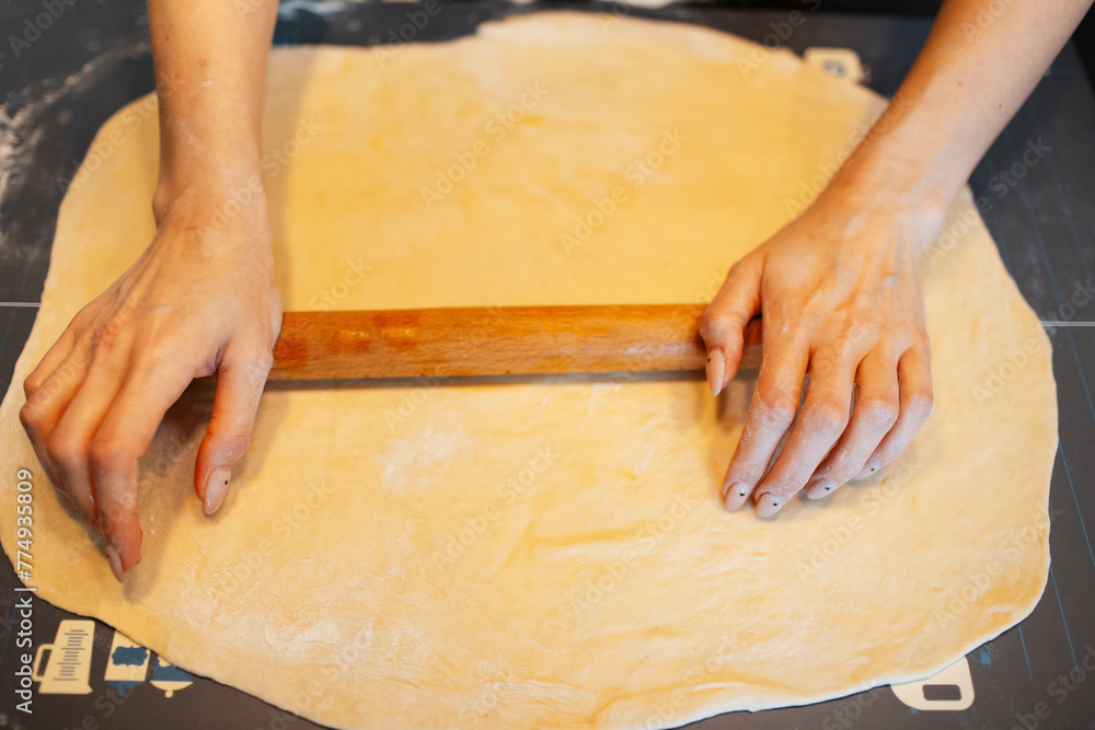 Top view of anonymous person hands rolling soft dough by rolling pin on table. Top view of anonymous person hands rolling soft dough by rolling pin on table.