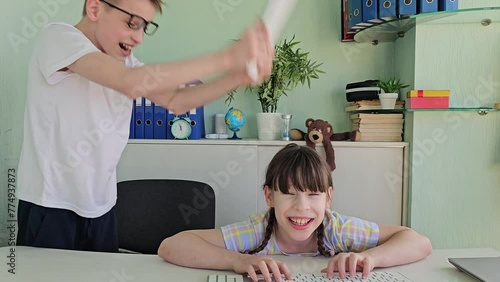 Girl child teenager furiously swings keyboard, hitting friend of classmate on the head in anger and disappointment, demonstrating violence at school. Children brother sister swear computer addiction o photo