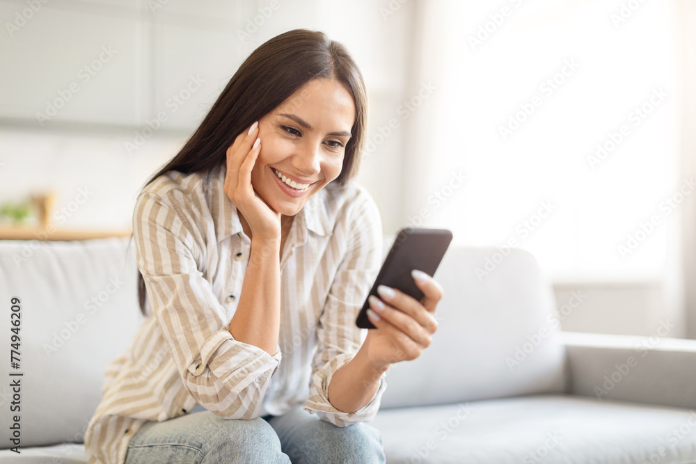 Relaxed woman smiling with smartphone at home Relaxed woman smiling with smartphone at home