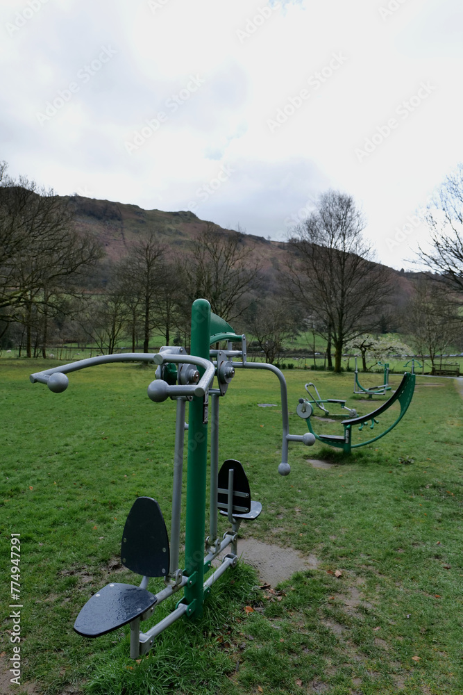 Fototapeta premium Exercise machines lined up in a public park with hills and trees in the background
