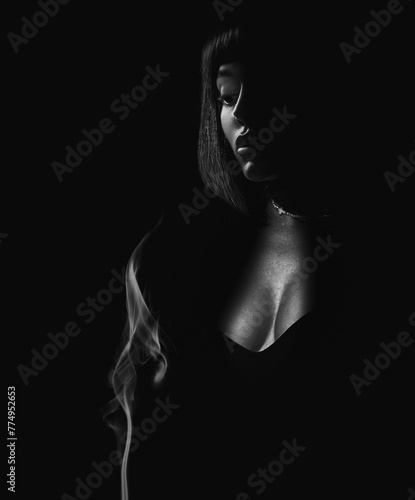 Portrait of a beautiful brunette girl with a French bob hairstyle with a catholic christian cross on the dark background with smoke. Conceptual black and white beauty close-up portrait.