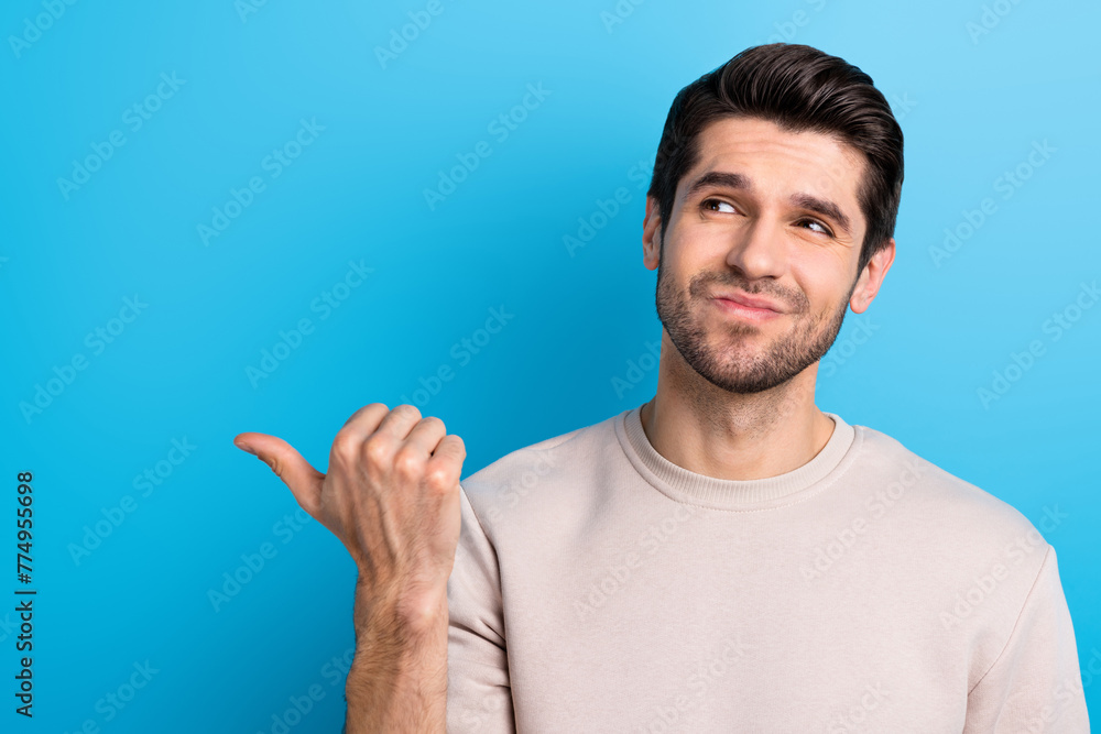 Portrait of minded intelligent guy with brunet hair wear light pullover look indicating empty space isolated on blue color background Portrait of minded intelligent guy with brunet hair wear light pullover look indicating empty space isolated on blue color background