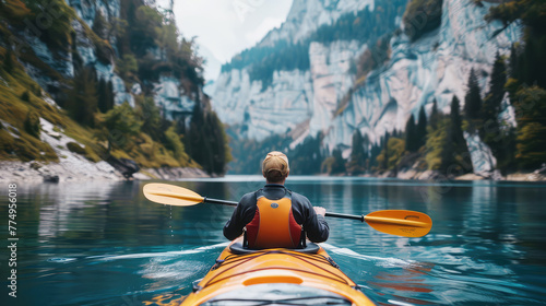 rear view of a man on a kayak floating on a serene mountain lake surrounded by steep cliffs and forest