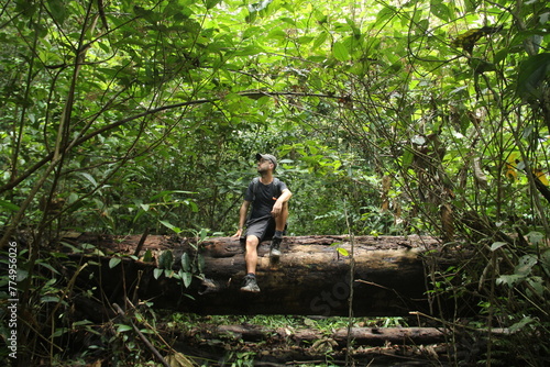 homem sentado em tronco caído em área de floresta amazônica, no amapá 