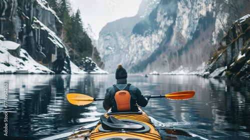 rear view of a man paddling a kayak in winter on a mountain lake surrounded by snow-covered rocks photo