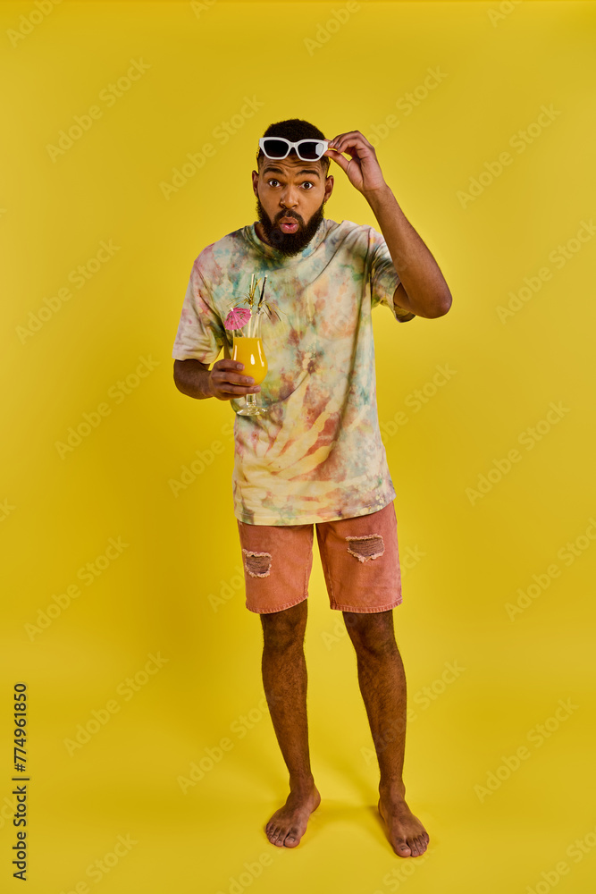 Fototapeta premium A stylish man in a vibrant tie dye shirt is holding a refreshing drink in his hand, exuding a carefree and relaxed vibe.