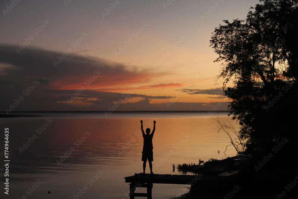 silhueta de homem na beira de rio no pôr do sol 