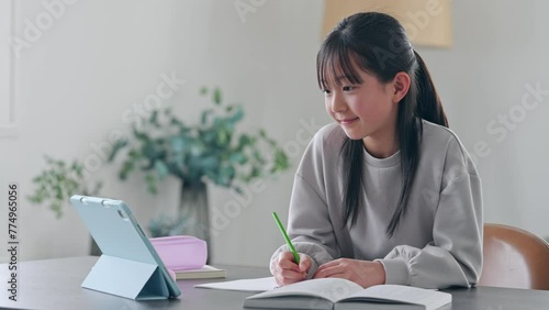 Elementary school girl studying at her desk at home while looking at a tablet PC. photo